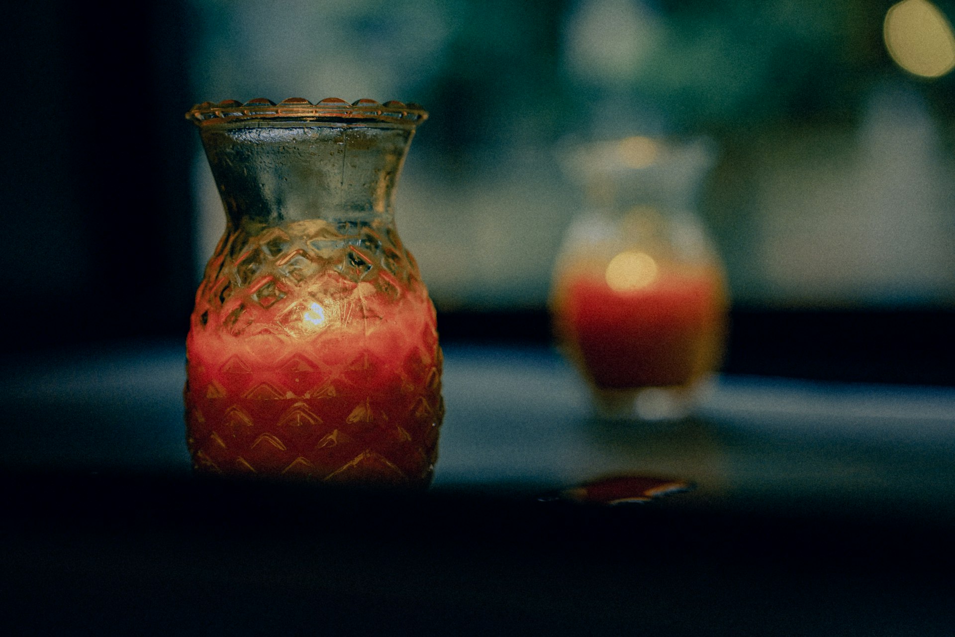 a red vase sitting on top of a table next to a glass